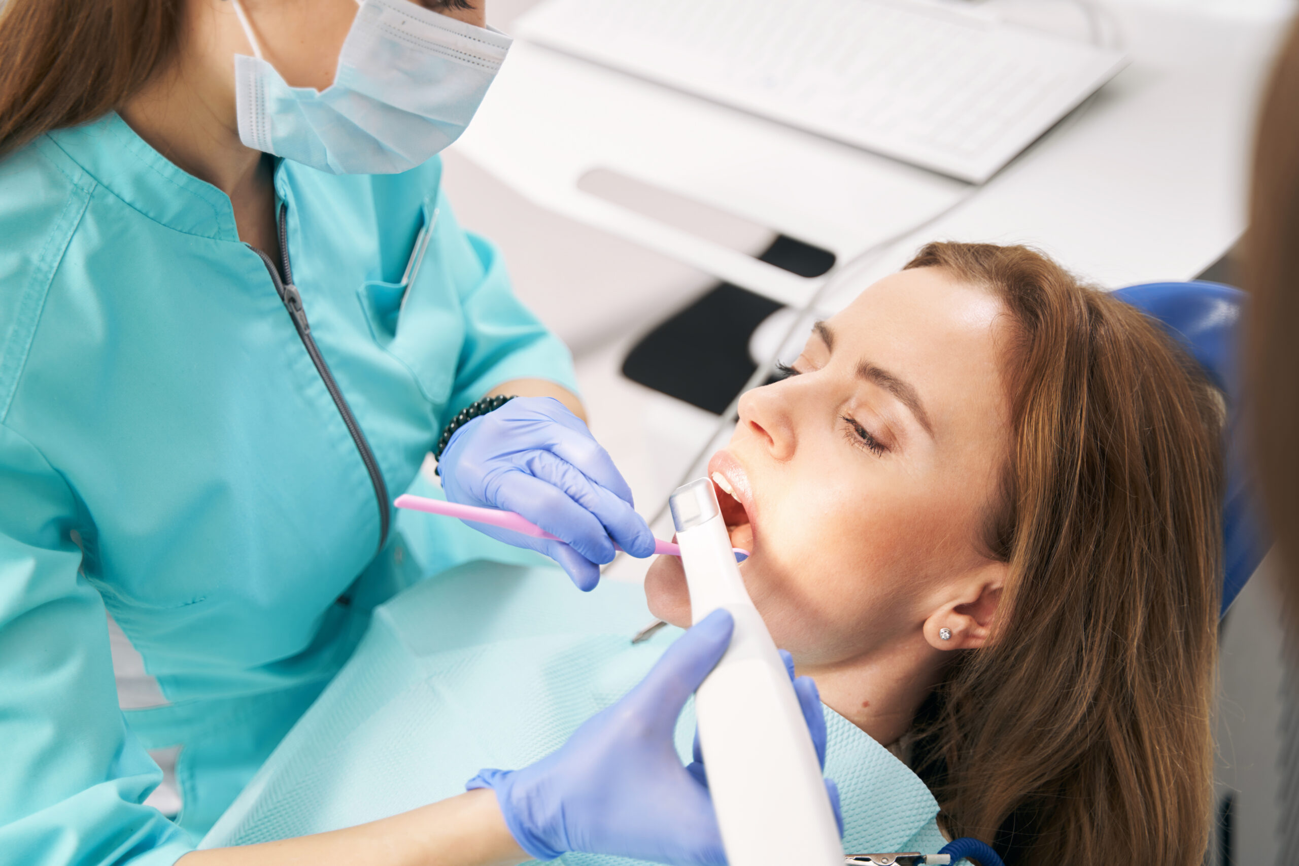 Doctor stomatologist examining female teeth with dental mirror and intraoral scanning device in stomatology clinic